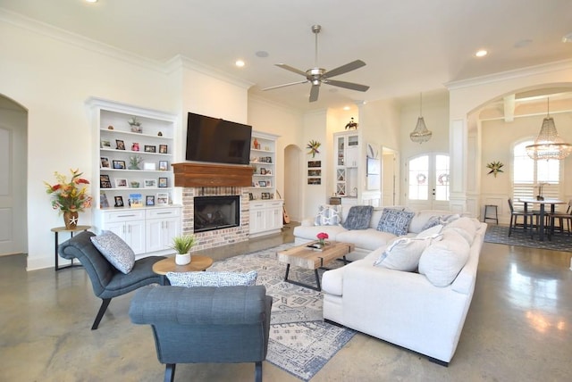 living room featuring built in shelves, ceiling fan with notable chandelier, concrete flooring, crown molding, and a brick fireplace