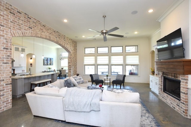 living room with crown molding, sink, a brick fireplace, ceiling fan, and brick wall