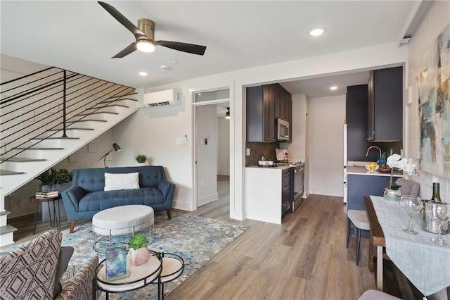 living room featuring a wall unit AC, ceiling fan, sink, and light hardwood / wood-style floors