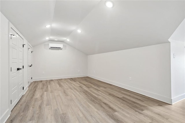 bonus room with an AC wall unit, vaulted ceiling, and light wood-type flooring