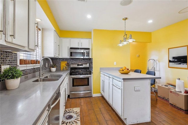 kitchen featuring stainless steel appliances, dark wood-type flooring, sink, hanging light fixtures, and white cabinetry