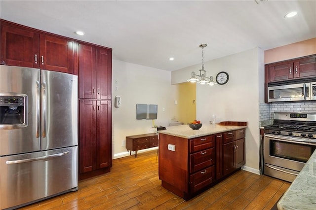 kitchen featuring light stone counters, dark hardwood / wood-style floors, tasteful backsplash, hanging light fixtures, and appliances with stainless steel finishes