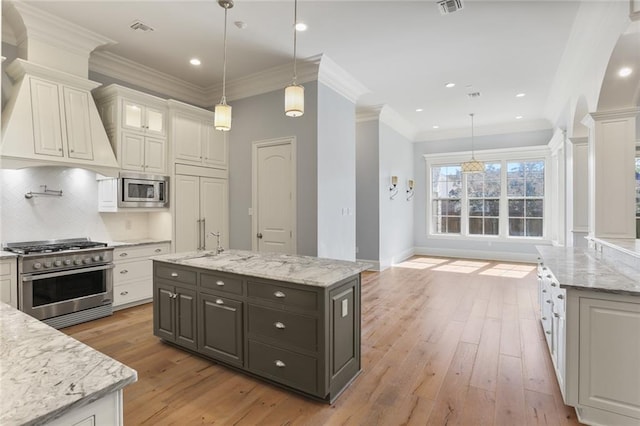 kitchen with appliances with stainless steel finishes, decorative columns, hanging light fixtures, and white cabinetry