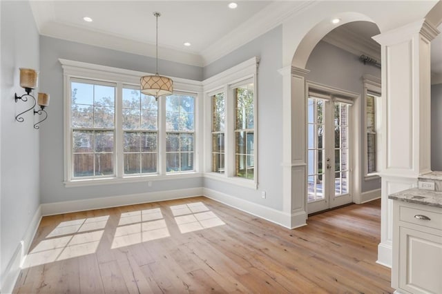 unfurnished dining area featuring ornate columns, light wood-type flooring, and a wealth of natural light