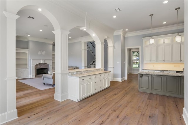 kitchen featuring light stone counters, white cabinets, pendant lighting, light hardwood / wood-style flooring, and ornamental molding