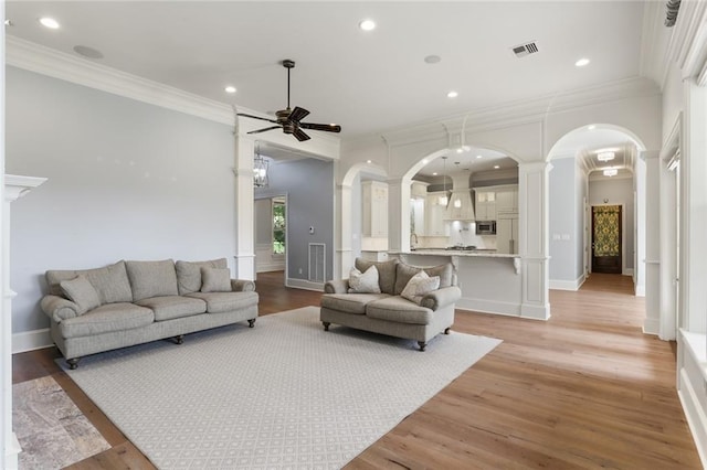 living room featuring ornate columns, ornamental molding, light wood-type flooring, and ceiling fan