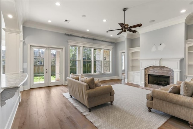 living room featuring ceiling fan, ornate columns, a high end fireplace, light hardwood / wood-style flooring, and ornamental molding