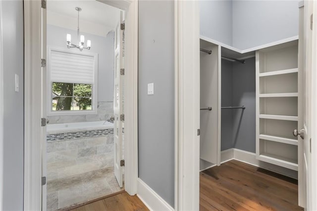 bathroom with hardwood / wood-style flooring, a notable chandelier, and a relaxing tiled tub