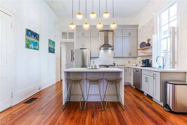 kitchen featuring dark wood-type flooring, stainless steel appliances, wall chimney range hood, backsplash, and a kitchen island