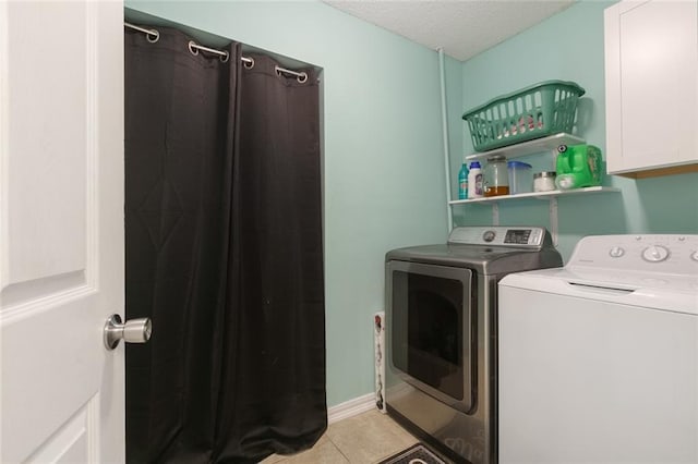 laundry area featuring cabinets, light tile patterned floors, a textured ceiling, and washing machine and clothes dryer