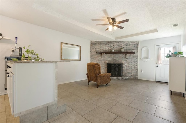 unfurnished living room featuring ceiling fan, a textured ceiling, a tray ceiling, a fireplace, and light tile patterned flooring