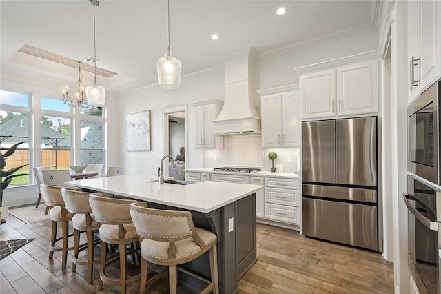 kitchen with stainless steel appliances, a kitchen island with sink, white cabinets, and premium range hood