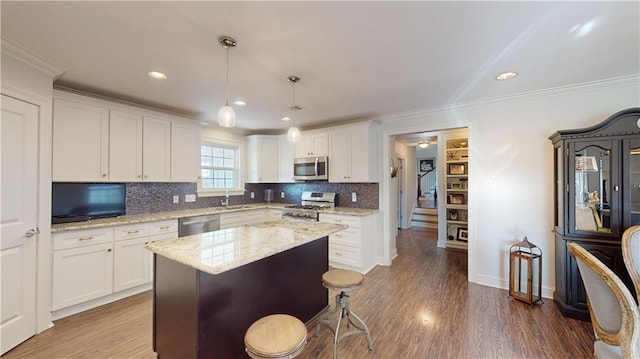 kitchen with a kitchen island, light stone counters, pendant lighting, white cabinetry, and appliances with stainless steel finishes