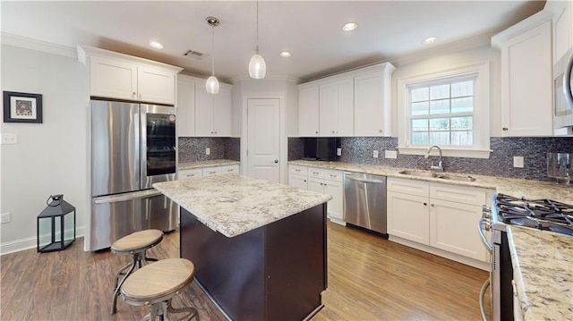 kitchen featuring hardwood / wood-style floors, white cabinets, sink, appliances with stainless steel finishes, and decorative light fixtures