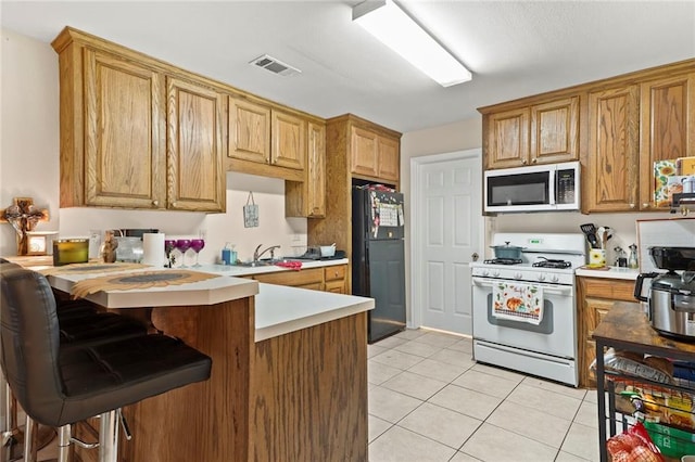 kitchen featuring white gas range, black refrigerator, light tile patterned flooring, kitchen peninsula, and a breakfast bar area