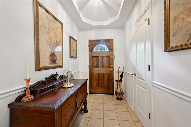 doorway to outside with crown molding, a tray ceiling, and light tile patterned floors