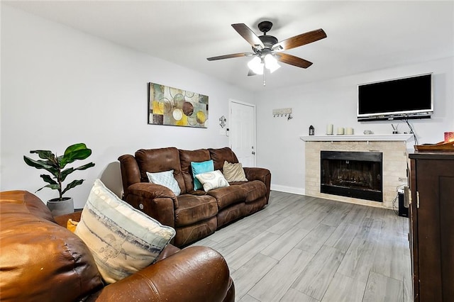 living room featuring a tiled fireplace, light hardwood / wood-style floors, and ceiling fan