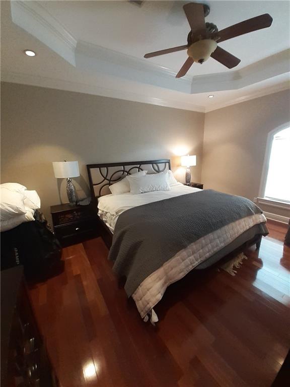 bedroom featuring a raised ceiling, dark hardwood / wood-style floors, ornamental molding, and ceiling fan