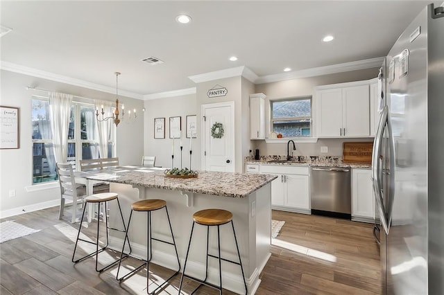 kitchen with a kitchen island, light wood-type flooring, sink, hanging light fixtures, and appliances with stainless steel finishes