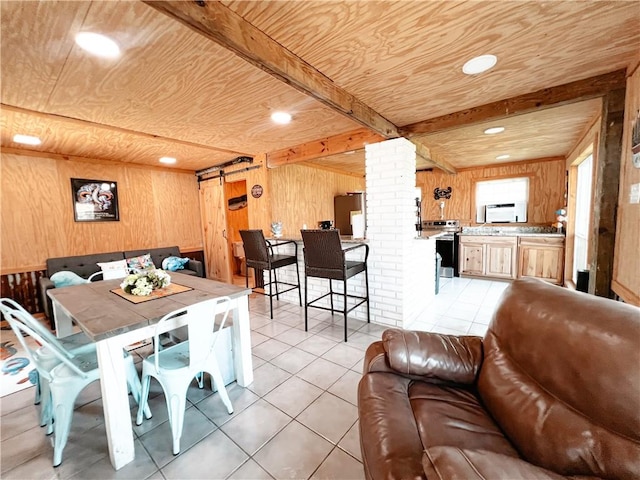 dining space with beamed ceiling, light tile patterned flooring, wood walls, and a barn door