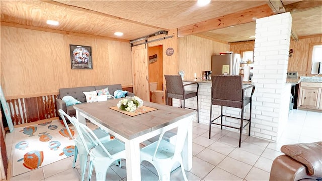 tiled dining space with ornate columns, wooden walls, beam ceiling, and a barn door