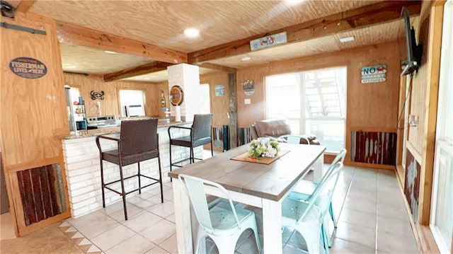 tiled dining room featuring beamed ceiling and wooden walls