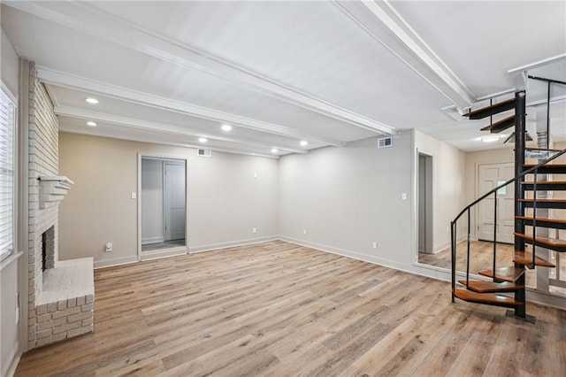 living room with a brick fireplace, beamed ceiling, elevator, and light hardwood / wood-style flooring