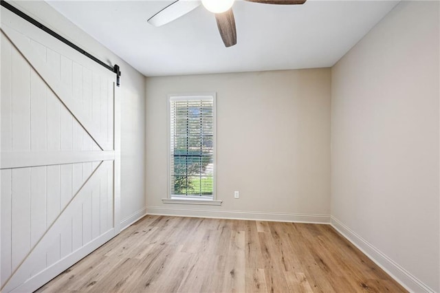 empty room with ceiling fan, light hardwood / wood-style flooring, and a barn door