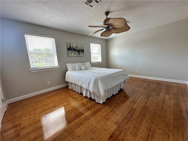 bedroom featuring a textured ceiling, hardwood / wood-style flooring, multiple windows, and ceiling fan