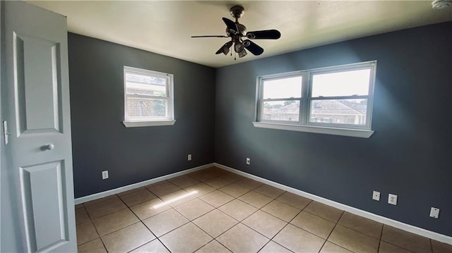 empty room featuring light tile patterned floors, a ceiling fan, and baseboards