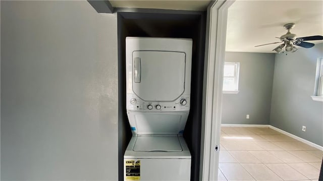 washroom with a ceiling fan, stacked washing maching and dryer, light tile patterned flooring, baseboards, and laundry area