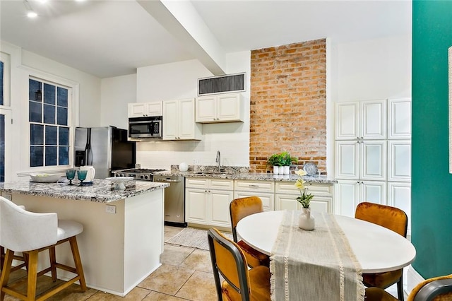 kitchen with a center island, light stone counters, white cabinets, light tile patterned floors, and appliances with stainless steel finishes