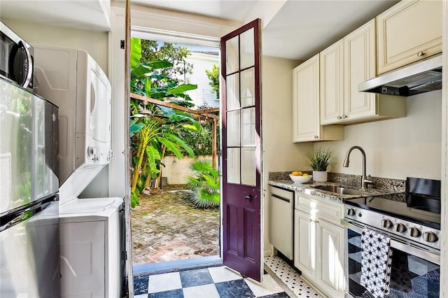 kitchen featuring stacked washing maching and dryer, light stone countertops, sink, and appliances with stainless steel finishes