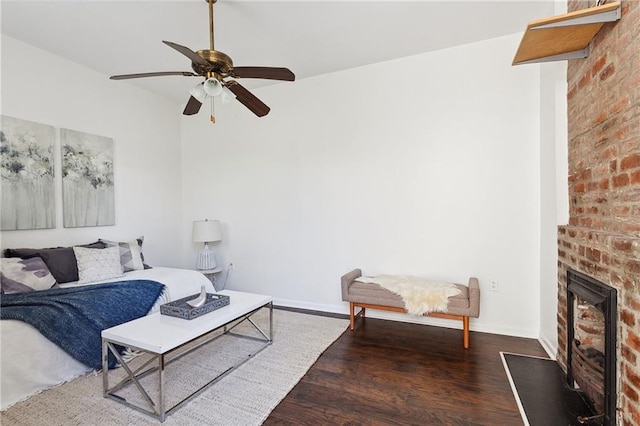 living room featuring dark wood-type flooring, ceiling fan, brick wall, and a brick fireplace