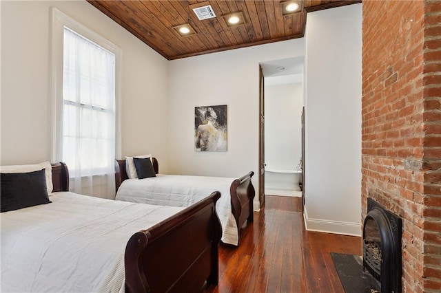 bedroom with brick wall, wood ceiling, crown molding, dark wood-type flooring, and a brick fireplace