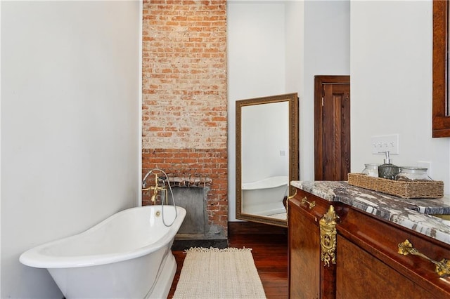 bathroom featuring vanity, hardwood / wood-style flooring, a brick fireplace, and a bathing tub