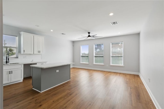 kitchen with ceiling fan, sink, a kitchen island, white cabinetry, and hardwood / wood-style floors