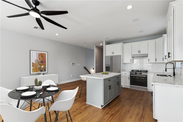 kitchen with sink, wood-type flooring, white cabinetry, appliances with stainless steel finishes, and a center island