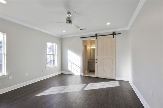 unfurnished room with ornamental molding, ceiling fan, a barn door, and dark hardwood / wood-style floors