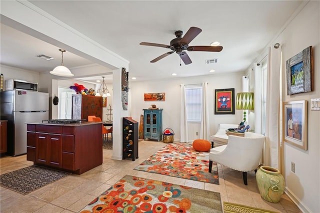 kitchen featuring light tile patterned flooring, ceiling fan with notable chandelier, crown molding, stainless steel appliances, and a center island