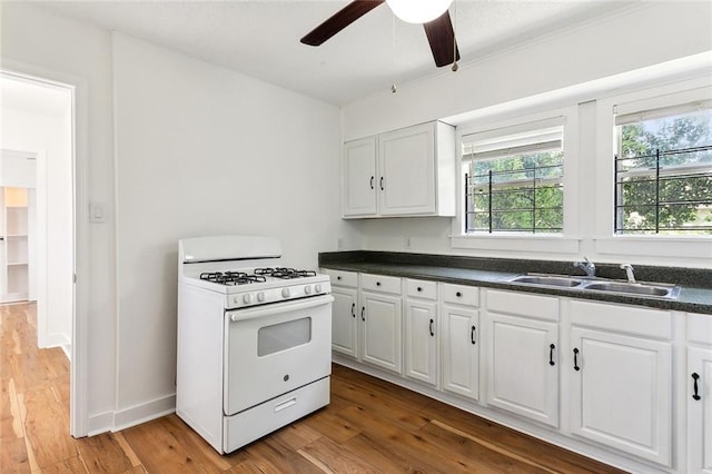 kitchen featuring ceiling fan, white cabinets, gas range gas stove, hardwood / wood-style flooring, and sink