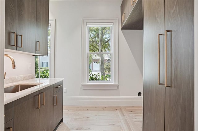 kitchen with plenty of natural light, dark brown cabinetry, a sink, and baseboards