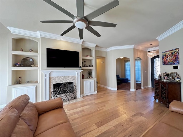 living room with light hardwood / wood-style floors, built in features, ceiling fan, crown molding, and a tiled fireplace