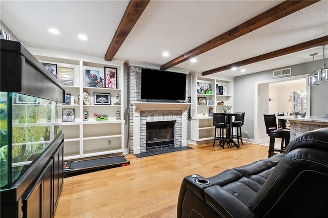 living room with a brick fireplace, beam ceiling, light hardwood / wood-style floors, and a textured ceiling