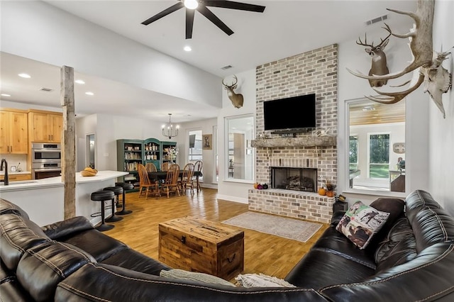 living room featuring ceiling fan with notable chandelier, a fireplace, light wood-type flooring, and sink