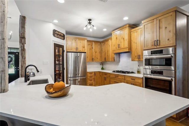 kitchen featuring light brown cabinets, a notable chandelier, sink, kitchen peninsula, and appliances with stainless steel finishes