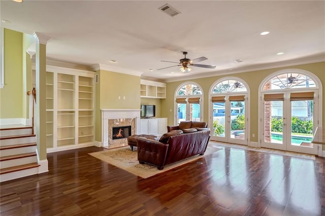 living room featuring ceiling fan, ornamental molding, french doors, dark wood-type flooring, and a fireplace