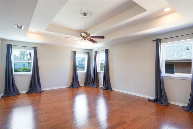 unfurnished room featuring a tray ceiling, plenty of natural light, and hardwood / wood-style floors