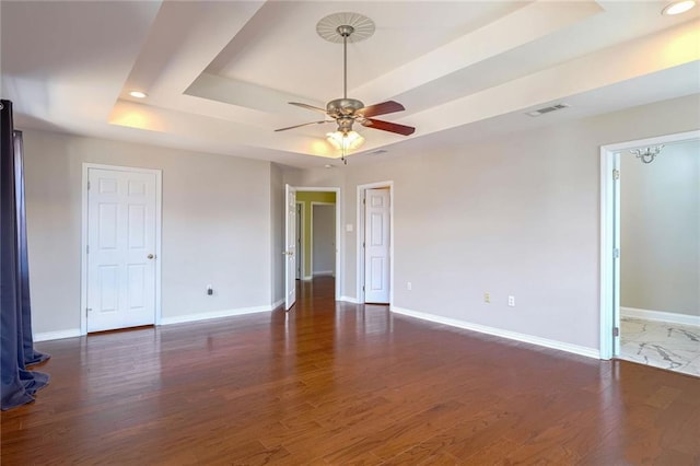 spare room featuring dark wood-type flooring, a tray ceiling, and ceiling fan