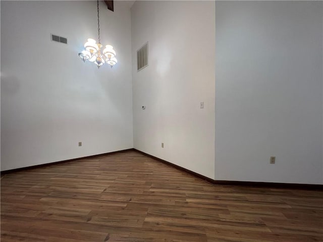 empty room featuring a towering ceiling, dark hardwood / wood-style floors, and an inviting chandelier